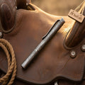 Minimalist Damascus ballpoint pen with monolithic forged-steel body on a western leather background