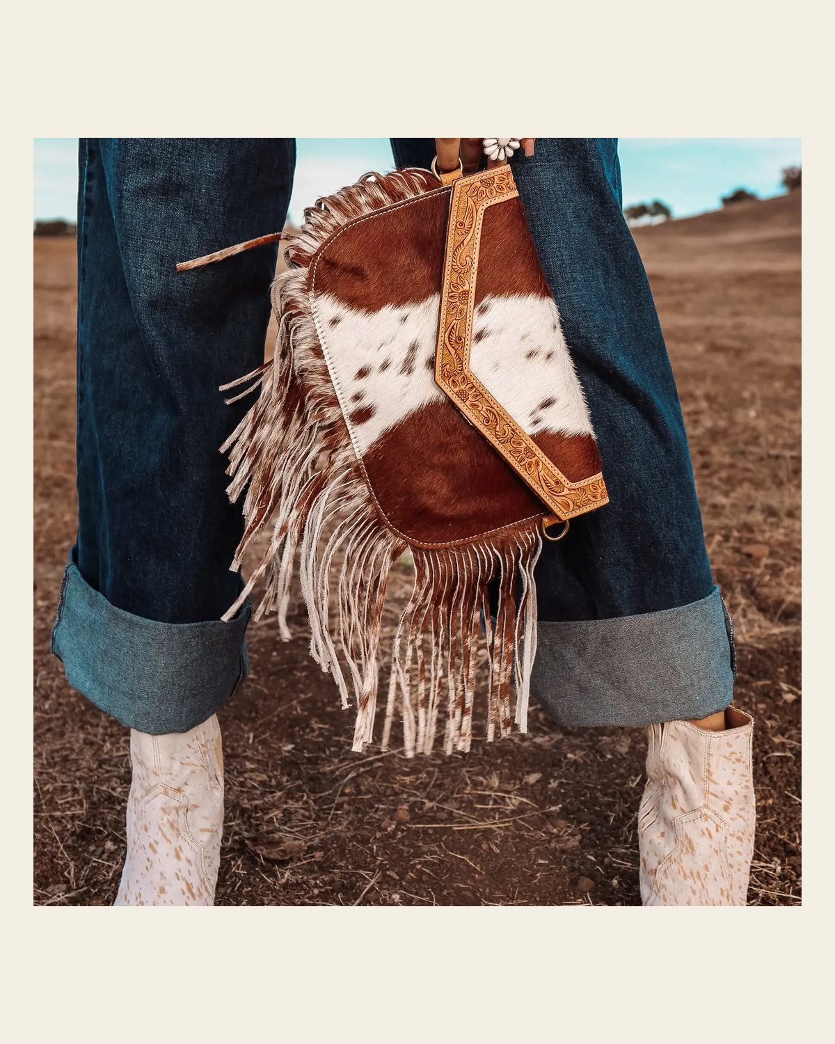 The Dallas Fringe Cowhide Leather Tooled Purse on a warm cream background
